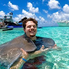 Cayman Adventure Tours guest holding a southern stingray in open water at the Stingray City sandbar in Grand Cayman